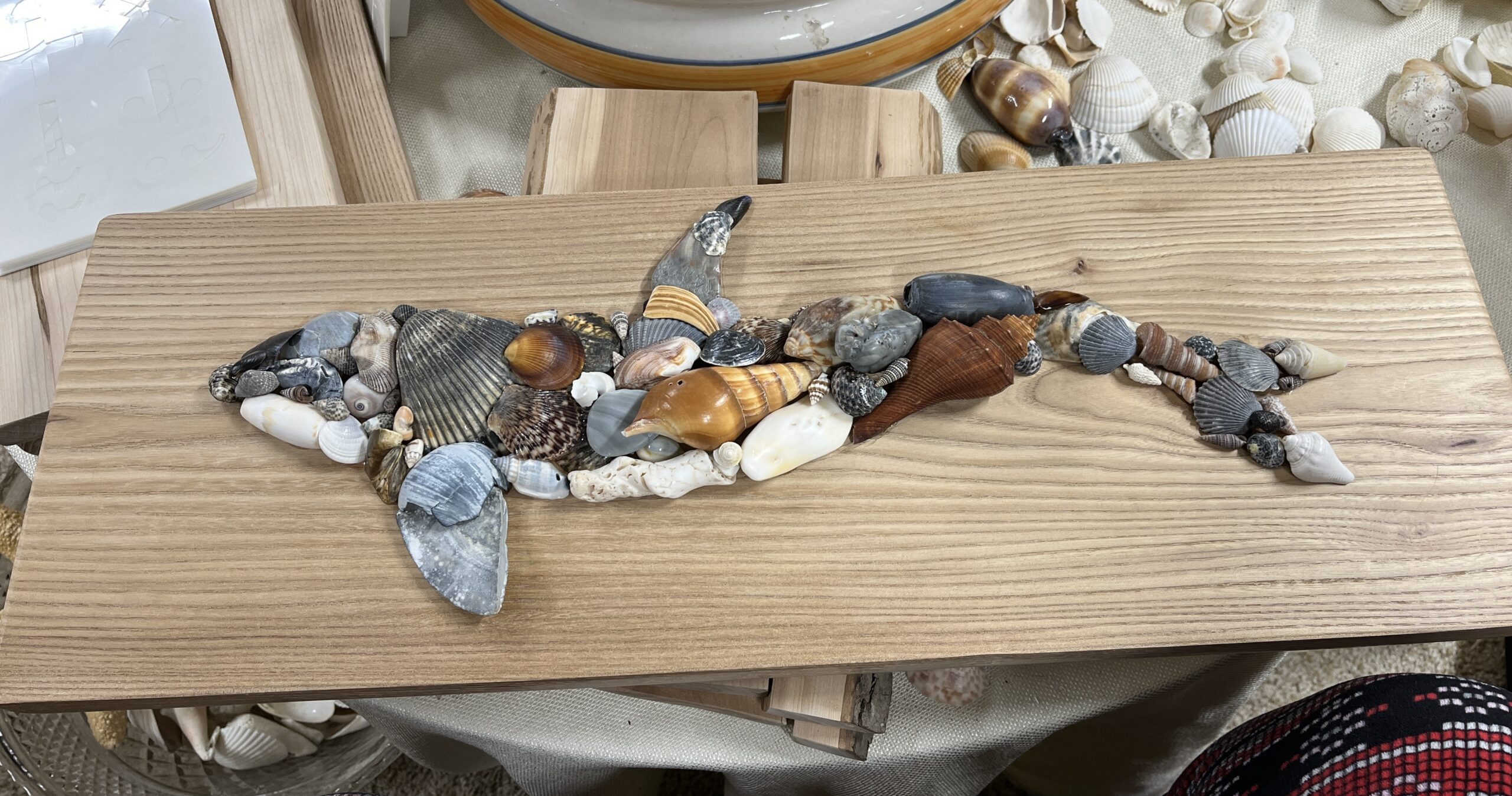 A whale design made of stones and shells on a wooden board.