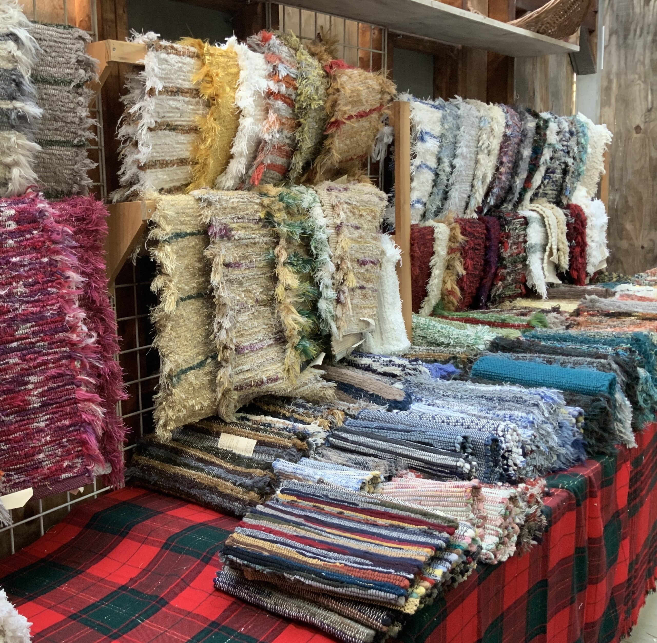 Hand-woven lamb rugs laid out on a table and draped on shelves on a wall.