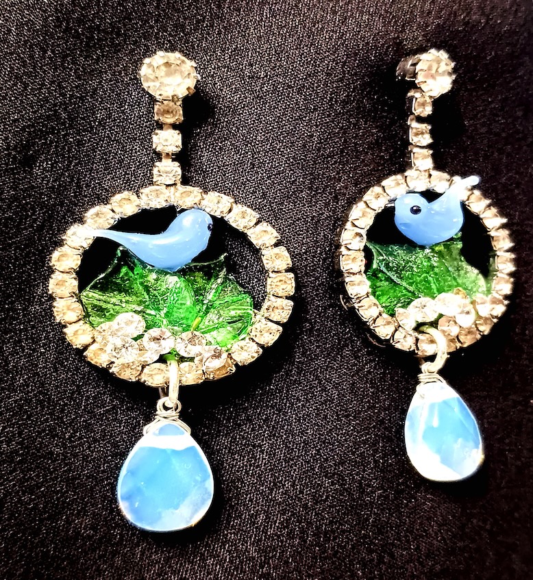 Two handmade earrings on a black cloth background.