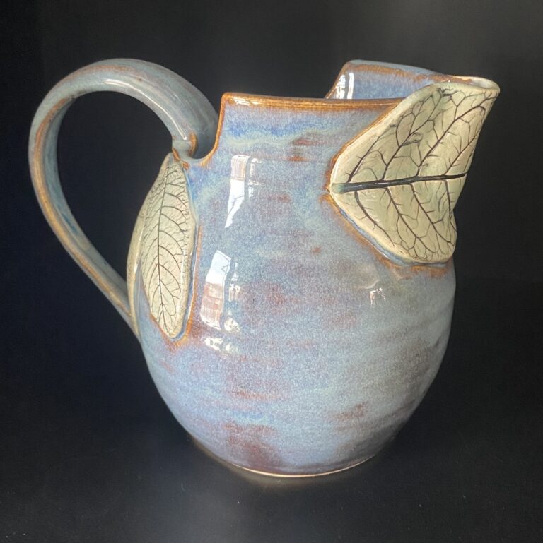 A clay mug with leaf-like designs on the sides.