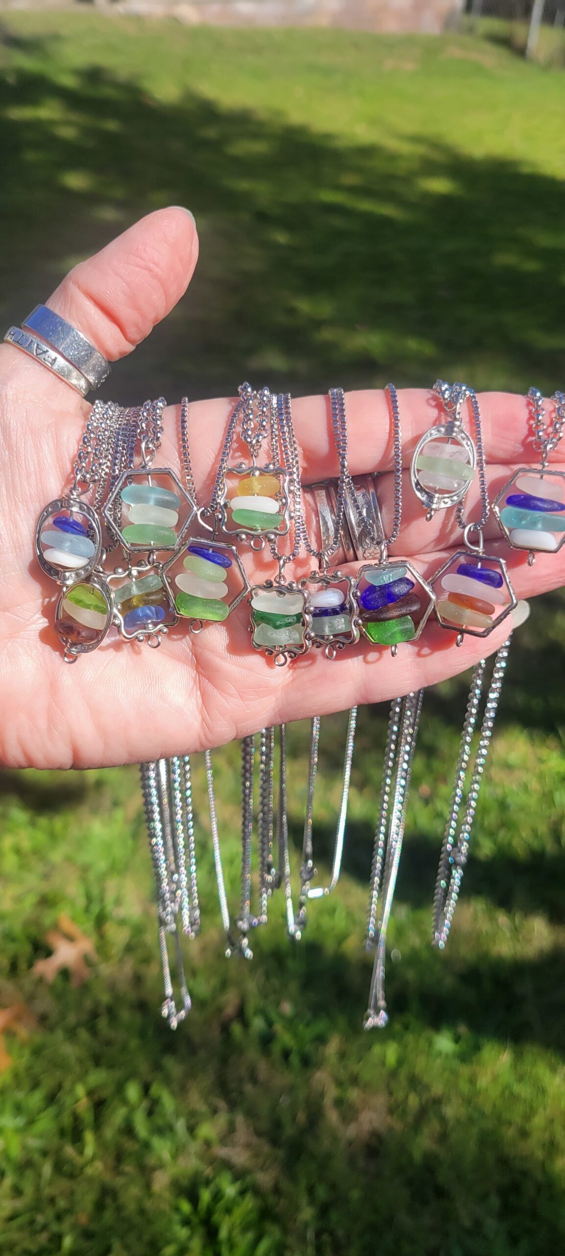 A hand holding numerous pieces of jewelry made of metal and beach glass.