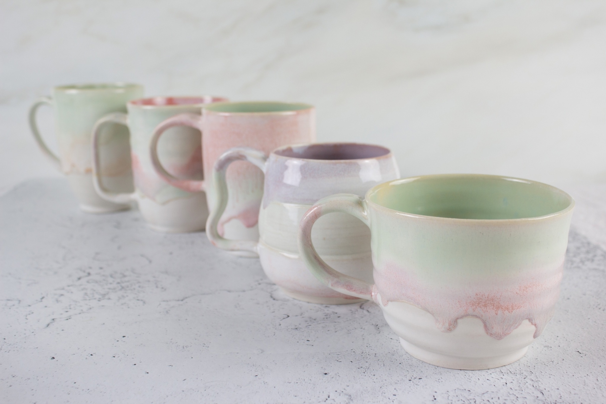 Five green and pink ceramic mugs lined up in front of a white marble backdrop.