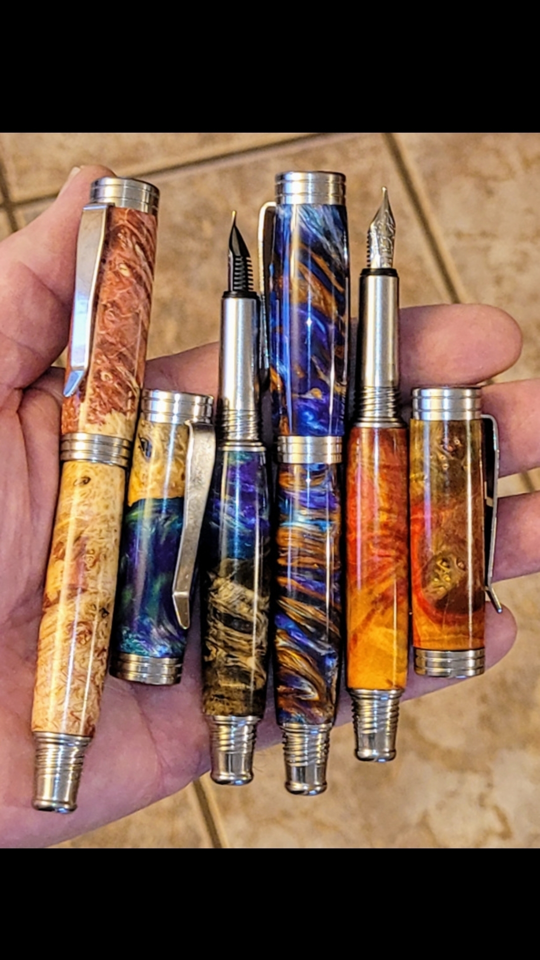 A hand holding a collection of handmade pens.