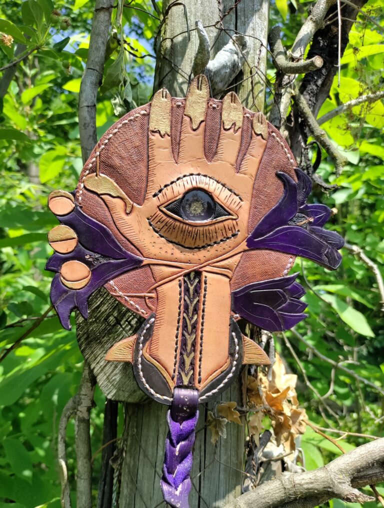 A handmade piece of leather art with a hand design in the center.